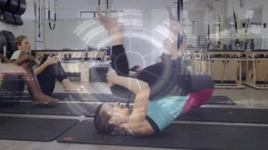 Turkuazlı kadın pilates minderinin üzerinde yuvarlanıyor, kaval kemikleri çekirdek olarak tutuluyor, dairesel atımlar yapıyor. Fitness, grup, stüdyo, reformcu, yalınayak, hareket, denge