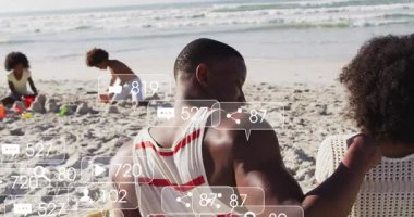 Sahilde oynayan çocukları izleyen bir adam, ortaya çıkan AR simgeleri, anlaşılması güç sahneler, pazarlamayı ön plana çıkaran. Aile, deniz kenarı, kumdan kale, çocuklar, açık hava, yaz, dinlenme