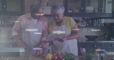 Kıdemli çift mutfakta yemek hazırlıyor, kadın tablet tıkırdatıyor oyun ikonlarının basamakları vurguluyor. Yaşlılar, aşçılar, mutfak, sebzeler, takım çalışması, dokunmatik ekran, ev yemeği