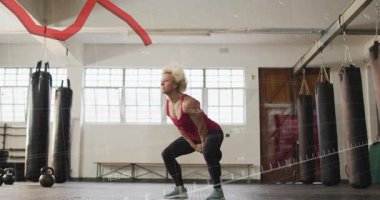 Kadın kafasının üstünden kettlebell indiriyor, menteşe takılıyor ve sallanırken kırmızı kaplama da fitness için iz sürme formu oluşturuyor. Spor, egzersiz, ağırlık, güç, antrenman, dinamik, odaklanma