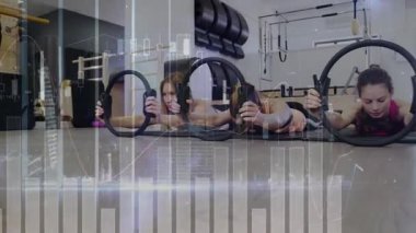 Antrenördeki spor salonundaki kadınlar göğüs kaldırıyor, halkaların altını çizerken yüzüklerin tonunu değiştiriyor. Pilates, grup, stüdyo, minderler, senkronizasyon, direniş, eğitmen
