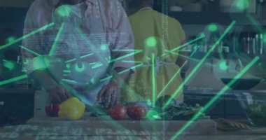 Kıdemli çift yemek hazırlıyor, yeşil düğümler ya da çizgiler sürüklenirken adam bıçağı kaldırıyor. Mutfak, sebze, önlük, çatal bıçak, tezgah, arkadaşlık, takım çalışması.