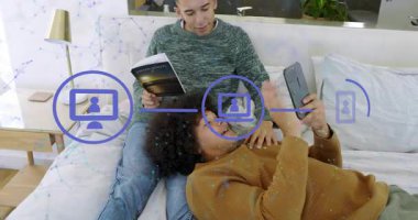 Arkaya yaslanan adam telefonu kaldırıyor, medyayı paylaşıyor, oturan adamın değişken bakışları, mavi teknolojiyle çifti örtüyor. Yatak odası, çift, rahat, rahat, kahkaha, akıllı telefon, okuma