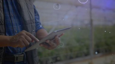 Seradaki tableti tıkırdatan yetişkin yetiştirici görüntülerini etkinleştirirken aynı zamanda görüntüyü de etkinleştiriyor. Bahçecilik, yenilik, teknoloji, kesinlik, sera, veri görselleştirme, sürdürülebilirlik