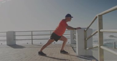Senior man walking onto boardwalk, initiating calf stretch for fitness warm-up with scrolling code. Outdoor, recreational, fitness, wellness, serene, technology, health