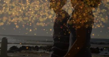 Walking on beach, people surrounded by golden light particles animation at sunset. relaxation, tranquility, seaside, golden hour, nature