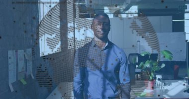 Standing Black man wearing light blue shirt in modern office, displaying dotted globe overlay. Workspace, analytics, double-exposure, open-plan, interior, monitor, notes