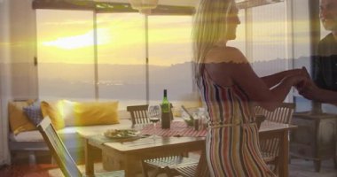 Neşeli bir şekilde dans eden çift, yemek masasında gün batımını seyrediyor. Romantik, akşam yemeği, ilişki, mutluluk, kutlama, eğlence