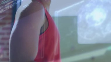 Erkek sporcu esniyor ve bilek takip cihazını çalıştırıyor, ısınırken projeksiyonları etkinleştiriyor. Fitness, giyilebilir, holografik, dijital, stüdyo, gün ışığı, odaklanma