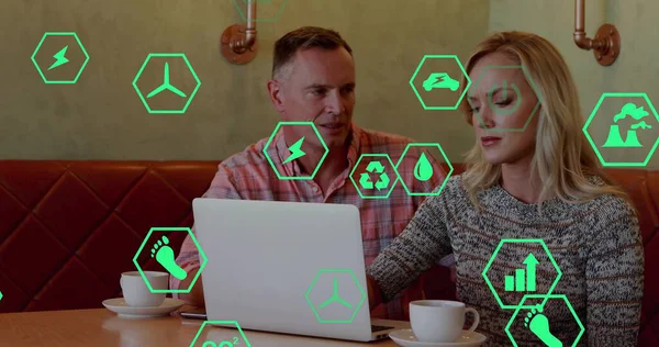 Yeşil ikonlar, beyaz dizüstü bilgisayarın üzerine eğilmiş bir çift kahve fincanları, kazak ve ekose gömlek. İşbirliği, işbirliği, sürdürülebilirlik, profesyoneller, tartışma, cihaz, kafe