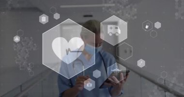 HUD çıktıktan sonra tablet kullanan kadın sağlık çalışanı, kalp fonksiyonlarını öne çıkaran ikonlar. Klinisyen, önlük, hastane, koridor, steteskop, maske, dokunmatik ekran.