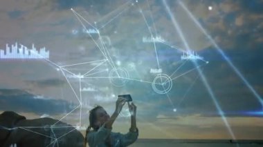 Technology researcher raising smartphone scanning horizon for coastal data with holographic charts. Futuristic, innovation, connectivity, exploration, data visualization, outdoor, research