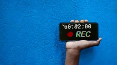 Akıllı telefon ekranında bulunan gizli kayıt mavi arkaplan 4K görüntüsünde izole edildi. Cep telefonunu elinde tutan ve gizli video ve ses kayıt seçeneğini gösteren kişi.