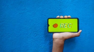 Akıllı telefon ekranında bulunan gizli kayıt mavi arkaplan 4K görüntüsünde izole edildi. Cep telefonunu elinde tutan ve gizli video ve ses kayıt seçeneğini gösteren kişi.