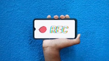 Akıllı telefon ekranında bulunan gizli kayıt mavi arkaplan 4K görüntüsünde izole edildi. Cep telefonunu elinde tutan ve gizli video ve ses kayıt seçeneğini gösteren kişi.