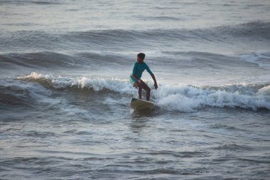 Kovalam, Chennai, Tamilnadu, Hindistan 9 Ağustos 2021 Hintli genç sörfçü ve plaj dalgalarında pratik yapıyor..