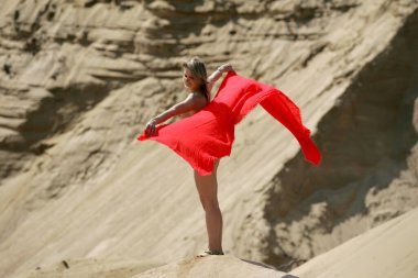 Güzel, çıplak bir kadın, arka planda kırmızı bir malzeme ile bir kum dağının arkasında poz veriyor.