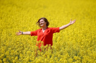 Kırmızı elbiseli mutlu bir genç kadın yaz mevsiminde tecavüz tarlasında eğleniyor. Petrol sahası olan kırsal bir arazi. Bahar çiçeği ve yağ. 