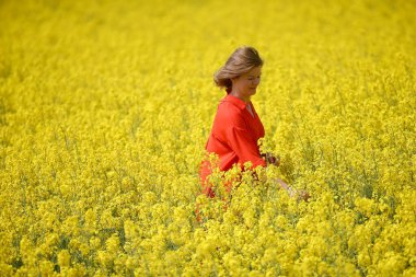 Kırmızı elbiseli mutlu bir genç kadın yaz mevsiminde tecavüz tarlasında eğleniyor. Petrol sahası olan kırsal bir arazi. Bahar çiçeği ve yağ. 