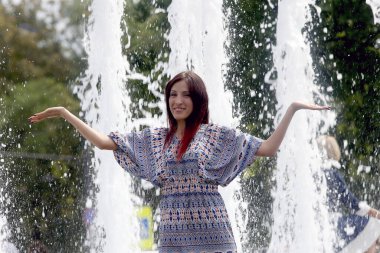 Güzel, genç bir kadın fıskiyenin arkasında poz veriyor.