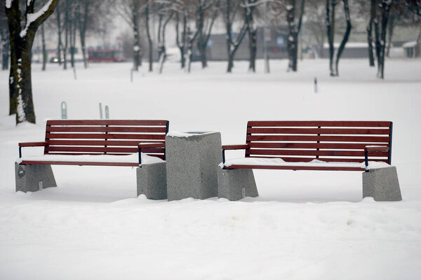 Benches for rest are covered with snow in the park in winter