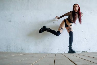 Fishnet kıyafetli gotik bir manken desenli beyaz bir duvara karşı anlamlı bir dans pozisyonu sergiliyor. Dinamik vücut dilini, dramatik duyguyu ve sanatsal performansı gösteren alternatif tarz hareket fotoğrafçılığı