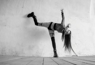 Fishnet kıyafetli gotik bir manken desenli beyaz bir duvara karşı anlamlı bir dans pozisyonu sergiliyor. Dinamik vücut dilini, dramatik duyguyu ve sanatsal performansı gösteren alternatif tarz hareket fotoğrafçılığı