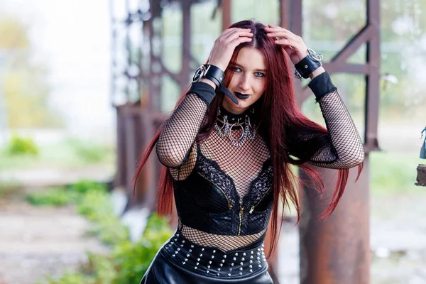 Uzun kızıl saçlı, siyah deri elbiseli ve siyah makyajlı gotik bir manken endüstriyel bir ortamda poz veriyor. Kendine güveni tam bir kadın portresi keskin güzelliğini ve karanlık estetiğini ifade ediyor..