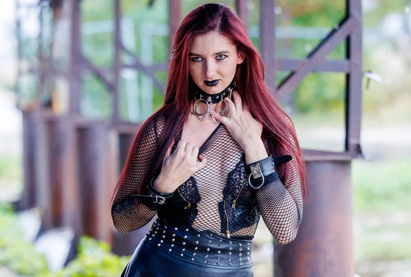 Uzun kızıl saçlı, siyah deri elbiseli ve siyah makyajlı gotik bir manken endüstriyel bir ortamda poz veriyor. Kendine güveni tam bir kadın portresi keskin güzelliğini ve karanlık estetiğini ifade ediyor..