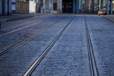 Yumuşak doğal ışıkta kaldırım taşlarından geçen tramvay raylarının yakın görüntüsü. Kalıplı taş kaldırım ve metal raylar soyut bir kentsel model oluşturur..