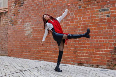 Dinamik portreler, arka planda tuğla bir sokakta dans eden bir kadının. Enerjik hareket, moda ayrıntıları ve açık havada doğal ışıkta yakalanan anlamlı hareket.