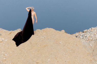 Doğada Zarafet: Karanlık Kumaşlı Bir Kadın Silueti Bir Arkaplan Su ve Kuma Karşı