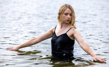 Siyah elbisesi dalgalanırken sakin suda zarif dans hareketleri yapan etkileyici genç bir kadın. Özgürlük kavramı, kadınlık, denge, duygusal ifade, beden farkındalığı ve doğa ile uyum.