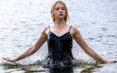 Siyah elbisesi dalgalanırken sakin suda zarif dans hareketleri yapan etkileyici genç bir kadın. Özgürlük kavramı, kadınlık, denge, duygusal ifade, beden farkındalığı ve doğa ile uyum.