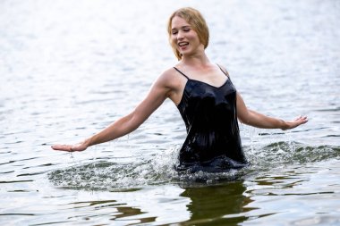 Siyah elbisesi dalgalanırken sakin suda zarif dans hareketleri yapan etkileyici genç bir kadın. Özgürlük kavramı, kadınlık, denge, duygusal ifade, beden farkındalığı ve doğa ile uyum.