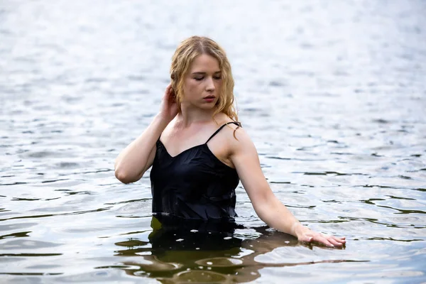 Siyah elbisesi dalgalanırken sakin suda zarif dans hareketleri yapan etkileyici genç bir kadın. Özgürlük kavramı, kadınlık, denge, duygusal ifade, beden farkındalığı ve doğa ile uyum.