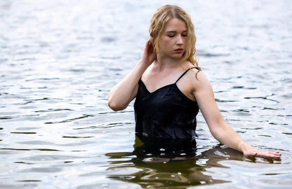 Siyah elbisesi dalgalanırken sakin suda zarif dans hareketleri yapan etkileyici genç bir kadın. Özgürlük kavramı, kadınlık, denge, duygusal ifade, beden farkındalığı ve doğa ile uyum.