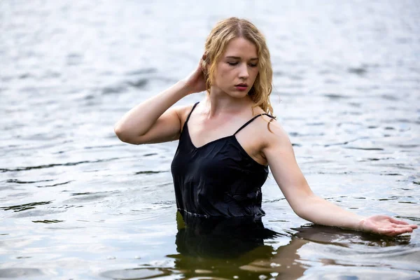 Siyah elbisesi dalgalanırken sakin suda zarif dans hareketleri yapan etkileyici genç bir kadın. Özgürlük kavramı, kadınlık, denge, duygusal ifade, beden farkındalığı ve doğa ile uyum.