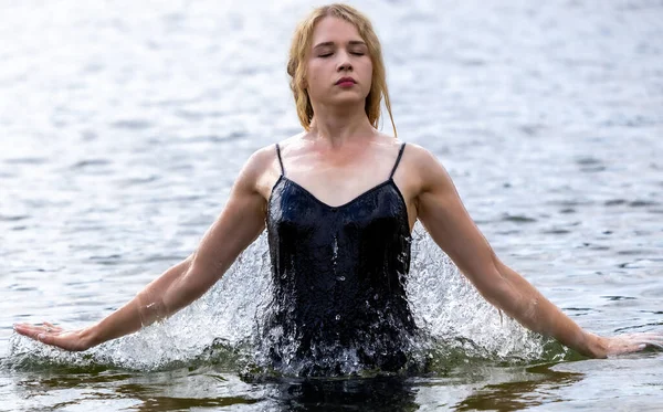 Siyah elbisesi dalgalanırken sakin suda zarif dans hareketleri yapan etkileyici genç bir kadın. Özgürlük kavramı, kadınlık, denge, duygusal ifade, beden farkındalığı ve doğa ile uyum.