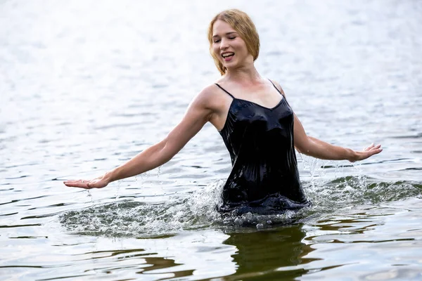 Siyah elbisesi dalgalanırken sakin suda zarif dans hareketleri yapan etkileyici genç bir kadın. Özgürlük kavramı, kadınlık, denge, duygusal ifade, beden farkındalığı ve doğa ile uyum.