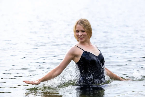 Siyah elbisesi dalgalanırken sakin suda zarif dans hareketleri yapan etkileyici genç bir kadın. Özgürlük kavramı, kadınlık, denge, duygusal ifade, beden farkındalığı ve doğa ile uyum.