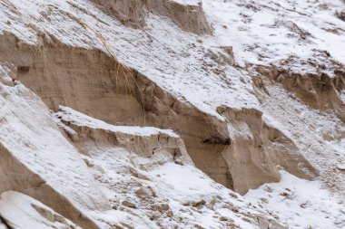 Taze karla kaplı aşınmış kum kayalıklarına yakın çekim. Doğal kış dokusu katmanlar, çatlaklar ve rüzgar ve hava tarafından şekillendirilen kırılgan yüzeyleri gösteriyor. Soyut arkaplan, jeoloji ve iklim kavramı.