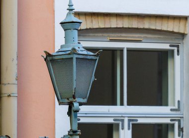 Tallinn Eski Kasabası 'ndaki tarihi sokak lambaları ve duvar fenerlerinin yakın çekimi, işlenmiş demir detaylar ve yumuşak kış ışığında klasik Avrupa mimarisi sergileniyor.