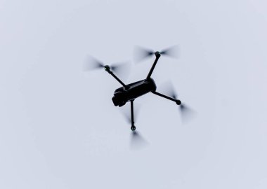 Kara kuadkopter drone silueti, yumuşak bulutlu bir gökyüzüne karşı, hareket bulanık pervaneler ve minimum arka plan gösteriyor, hava teknolojisi ve gözlem kavramları için uygun..