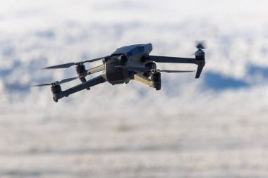 Hafif bulanık kış arkaplanı üzerinde uçan bir kameranın yakın görüntüsü, kolları, motorları ve pervaneleri gösteren, sığ alan derinliğine sahip, hava çekim ve modern teknoloji temaları için ideal.