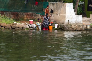 Allepey, Kerala, India, March 31, 2015:Unidentified indian woman wash their clothes in front of his house on the water clipart