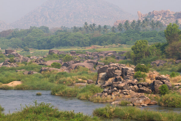 Hampi village Tungabhadra river meadow. Landscape with water, palm, rock, stones. India, Karnataka