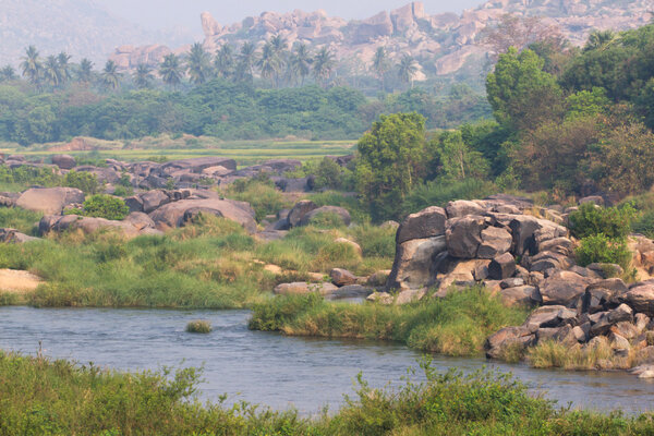 Hampi village Tungabhadra river meadow. Landscape with water, palm, rock, stones. India, Karnataka