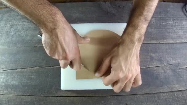 Proces produkcji skóry. Okrągłe cięcie kawałka skóry, tworzenie produktu. Domowej roboty. Drewno tło skóra produkcja z męski ręka. 4k, 30 klatek na sekundę. — Wideo stockowe