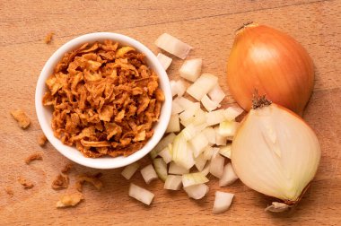 Beyaz seramik kasede kızarmış soğan, bir yığın taze doğranmış soğan ve ahşap tahtada yarım soğan. Üst görünüm..